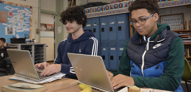 two high school boys working at computers in classsroom