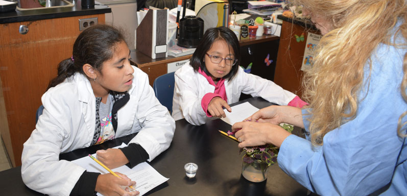 two female students working in a biology lab with female teacher